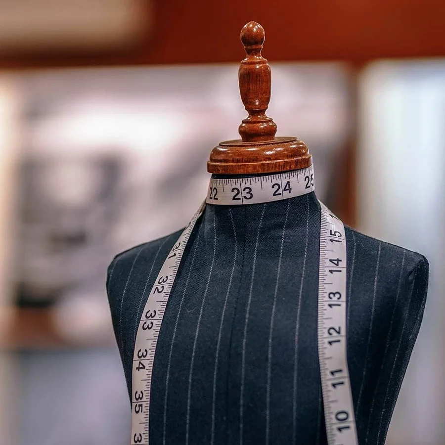 A dark pinstriped dress form with a measuring tape draped around its neck