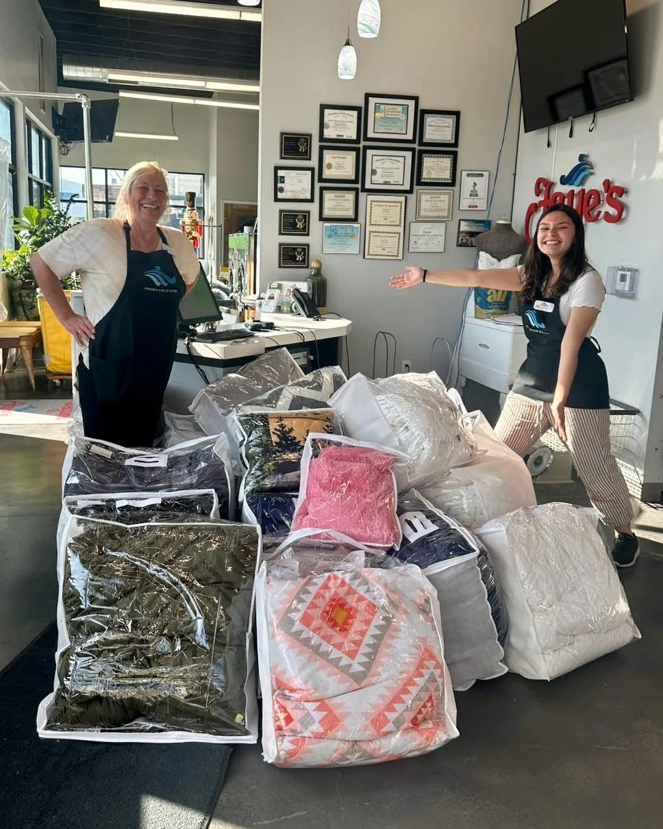 Two Faye's team members standing beside stacks of bagged comforters and quilts in the shop
