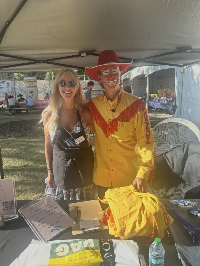 A rodeo performer in a yellow western shirt and red hat beside another person under a canopy