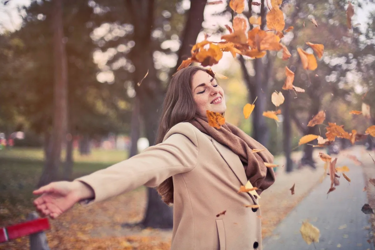 A woman in a tan wool coat standing among autumn leaves