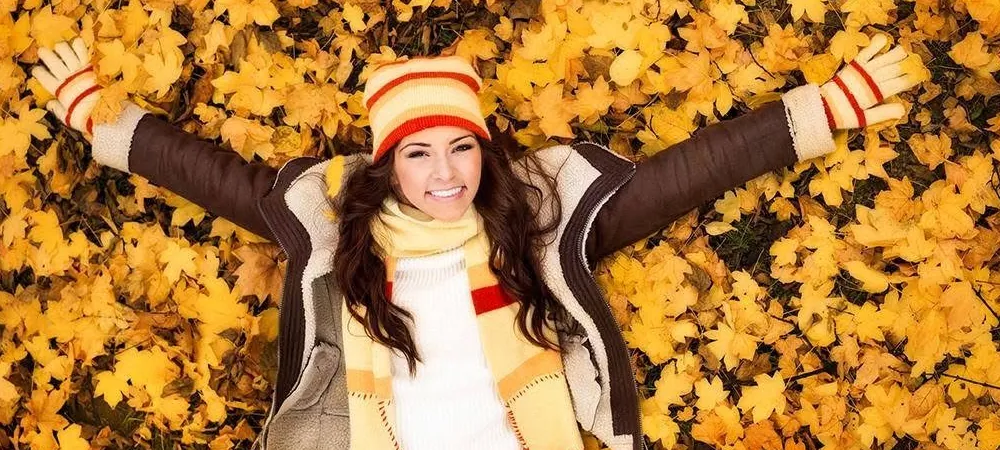 A woman in a jacket, scarf and striped hat lying in autumn leaves