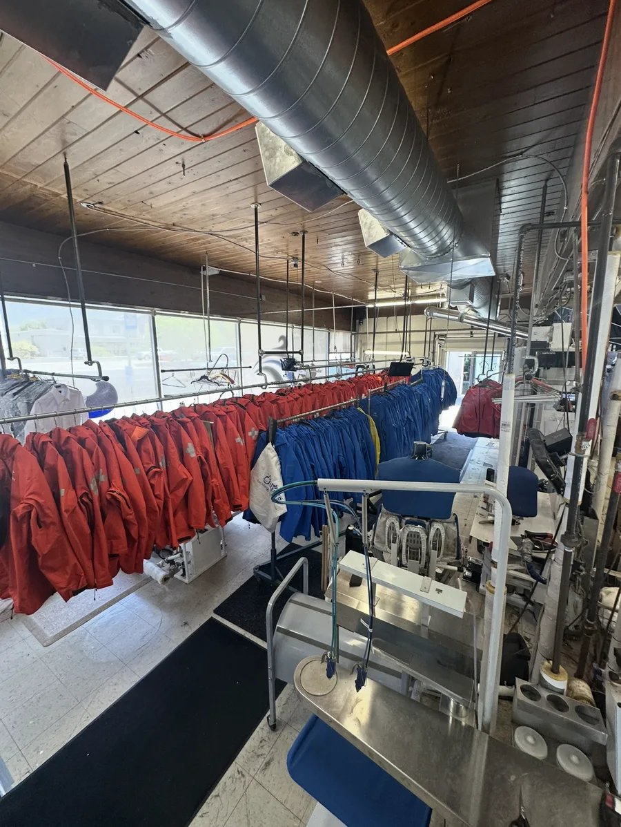 Rows of red and blue garments hanging beside pressing equipment inside Faye's cleaning facility