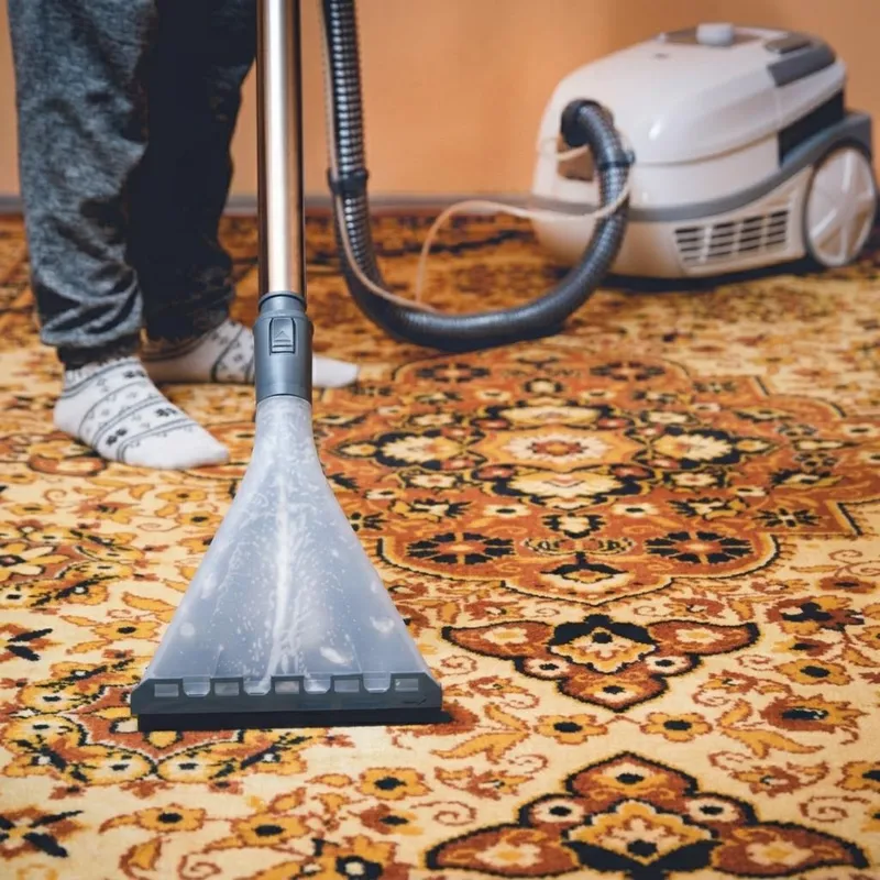 Clear extraction nozzle on a patterned orange and gold rug, with a cleaning machine in the background. Illustrative photo, not Faye's staff or equipment.